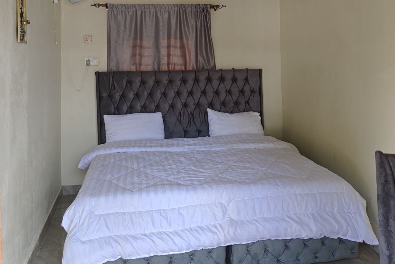 A neatly made bed with a tufted headboard, white bedding, and a grey curtain above.