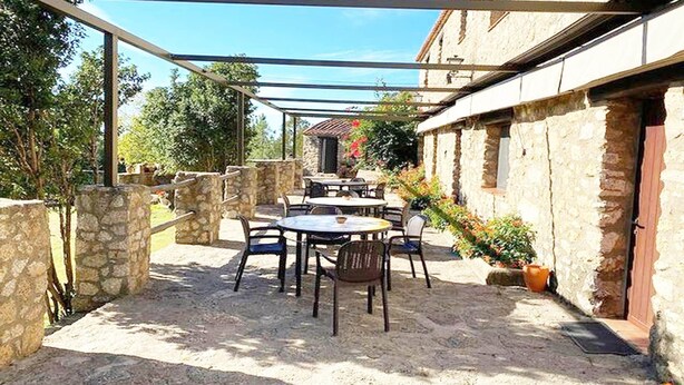Un patio exterior con paredes de piedra, una pérgola y una mesa con sillas.