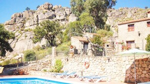Un edificio de piedra con piscina, sillones de descanso y un cerro rocoso al fondo.