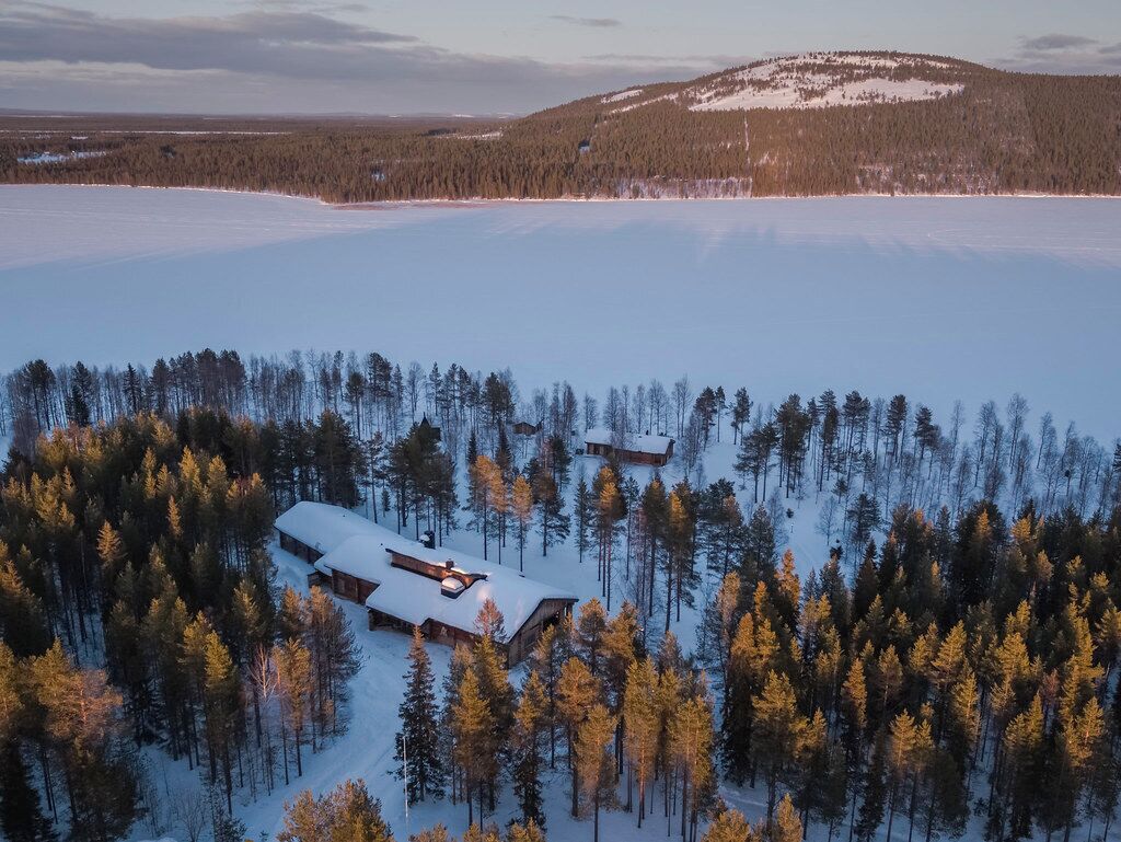 A cabin surrounded by a dense forest and a frozen lake.