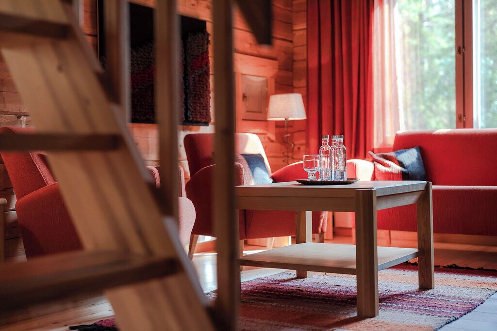 A cozy log cabin interior with a wooden table, red upholstered chairs, and a red sofa.