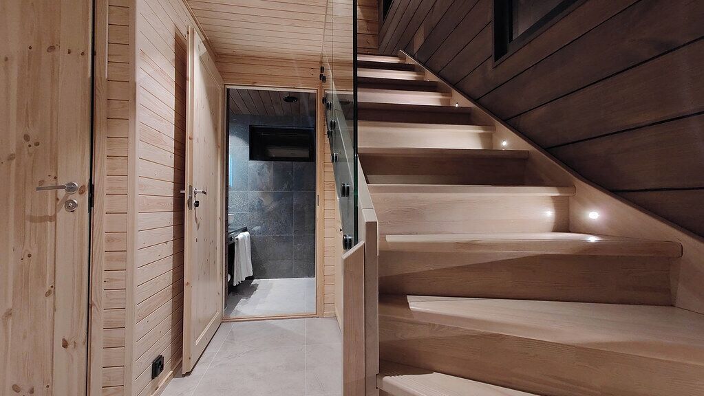 Una escalera de madera que conduce a un baño con puerta de cristal.