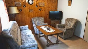 Un salon avec des canapés à motifs, un mur en bois, une télévision et une horloge.