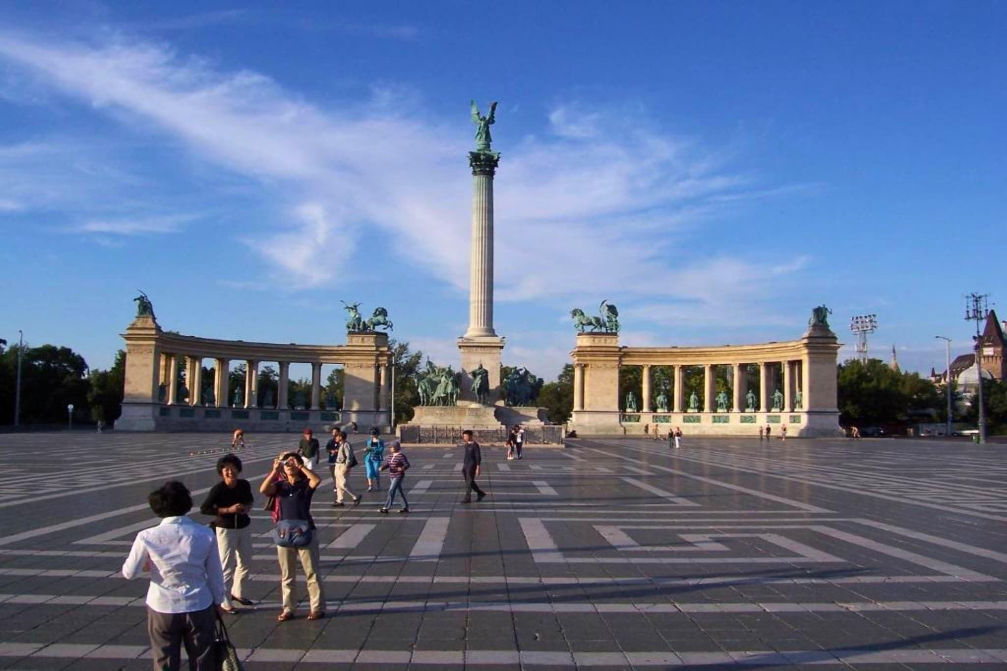 Una amplia plaza abierta con un monumento central y estatuas, rodeada de edificios.