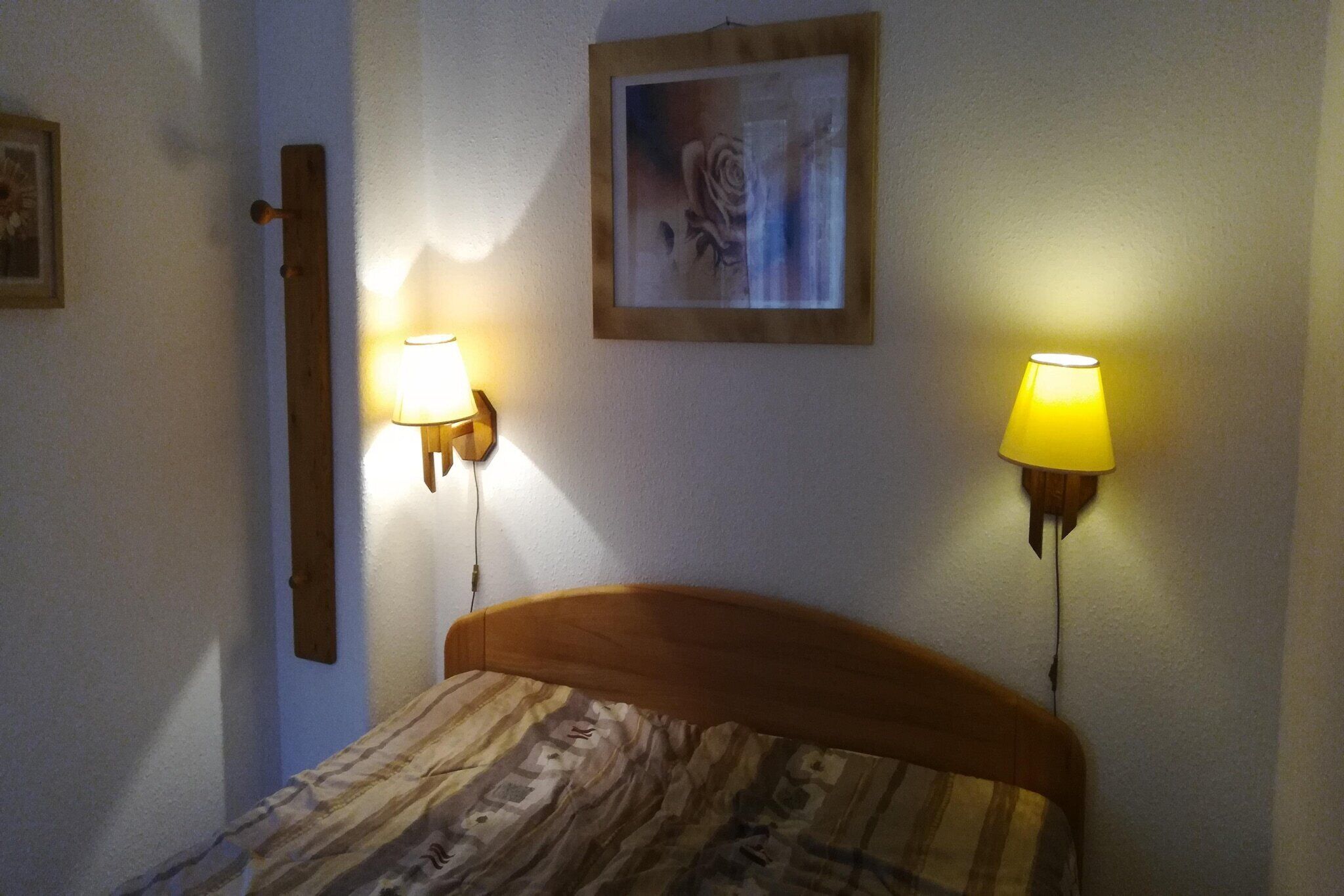 A bedroom with a wooden headboard, two wall-mounted lamps, and a framed picture on the wall.