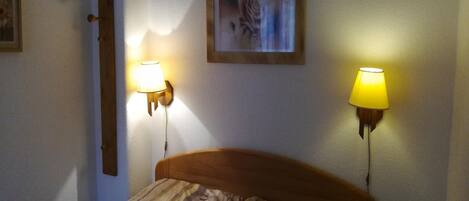 A bedroom with a wooden headboard, two wall-mounted lamps, and a framed picture on the wall.