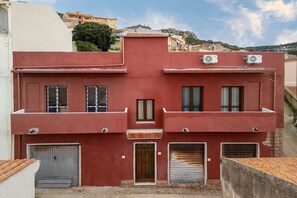 A red building with two air conditioning units, a central door, and two garage doors. - Appartamento con aria condizionata (Sassari)
