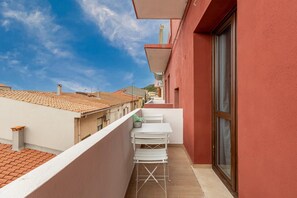 A balcony with a white table and chairs, a potted plant, and a view of neighboring buildings. - Appartamento con aria condizionata (Sassari)