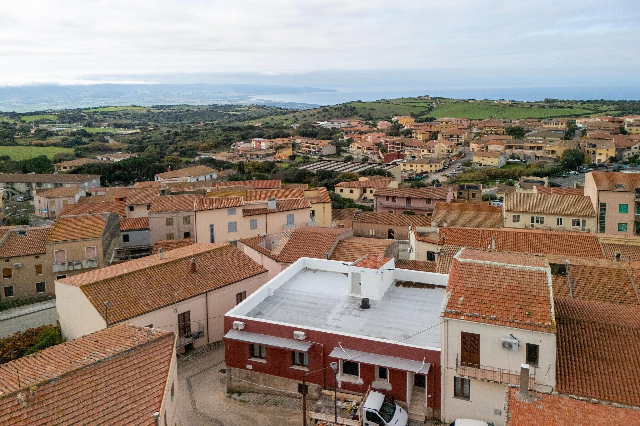 A residential area with terracotta-tiled roofs, a mix of single and multi-story buildings, and a distant view of the coastline.