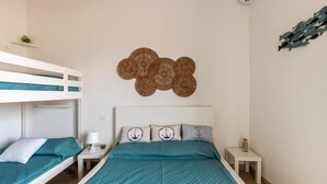 Een slaapkamer met stapelbedden, een bed met een blauwgroene sprei, en een wanddecoratie.