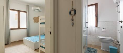 Un dormitorio con cama, ventana y puerta que da a un baño con inodoro y ducha.
