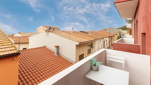 En boligbygning med terracotta tagsten, en balkon med en potteplante og en klar blå himmel.