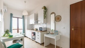 Et moderne køkken med hvide skabe, en mikrobølgeovn og en vask. Der er et spisebord med stole og et lille skrivebord med et spejl.