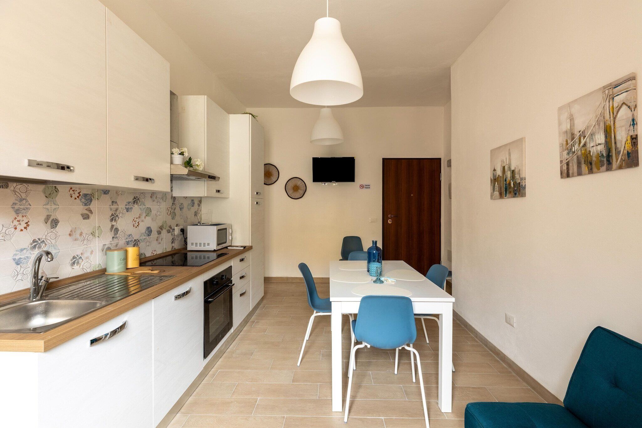 A modern kitchen with a white countertop, stainless steel sink, and a dining area with a white table and blue chairs.