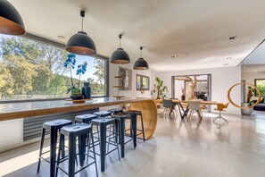 Uma cozinha moderna com banquetas, iluminação pendente e vista para o exterior.