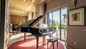 Un piano de cola imponente en una habitación amplia con alfombra roja, ventanas grandes y vistas al verdor exterior.
