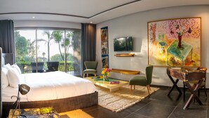 Habitación de hotel moderna con una cama grande, un escritorio, una silla, un televisor y obras de arte en las paredes.