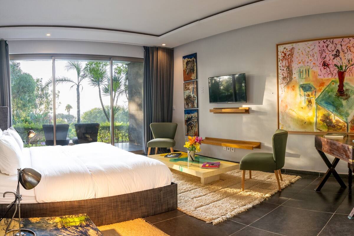 Habitación de hotel moderna con una cama grande, un escritorio, una silla, un televisor y obras de arte en las paredes.