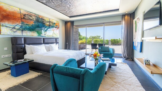 Una habitación de hotel moderna con una cama grande, un sofá, una mesa de centro y un balcón con vistas.