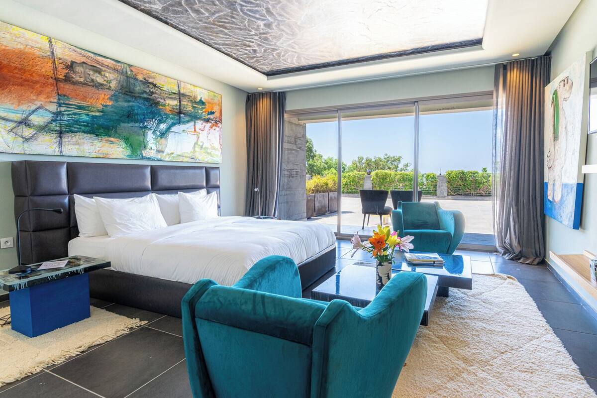 Una habitación de hotel moderna con una cama grande, un sofá, una mesa de centro y un balcón con vistas.