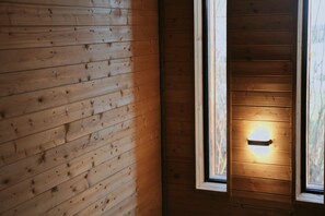 A wooden cabin interior with a window and a wall-mounted light fixture.