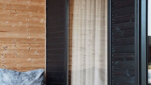 A room with a wooden wall, a black-framed table, a grey sofa, and a large window with a beige curtain. - Ranch In Variani (Variani)