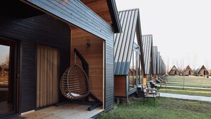 A modern building with a wooden exterior and metal sloped roofs. There is a hanging chair outside and several benches in the yard. - Ranch In Variani (Variani)