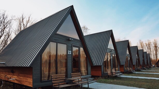 A row of modern, triangular-roofed cabins with large windows, numbered sequentially, and wooden benches outside. - Ranch In Variani (Variani)