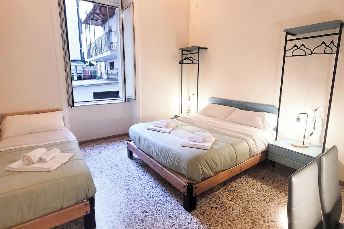 Ein Schlafzimmer mit einem Bett, zwei Nachttischen, einem Sessel und einem Fenster mit Blick nach draußen.