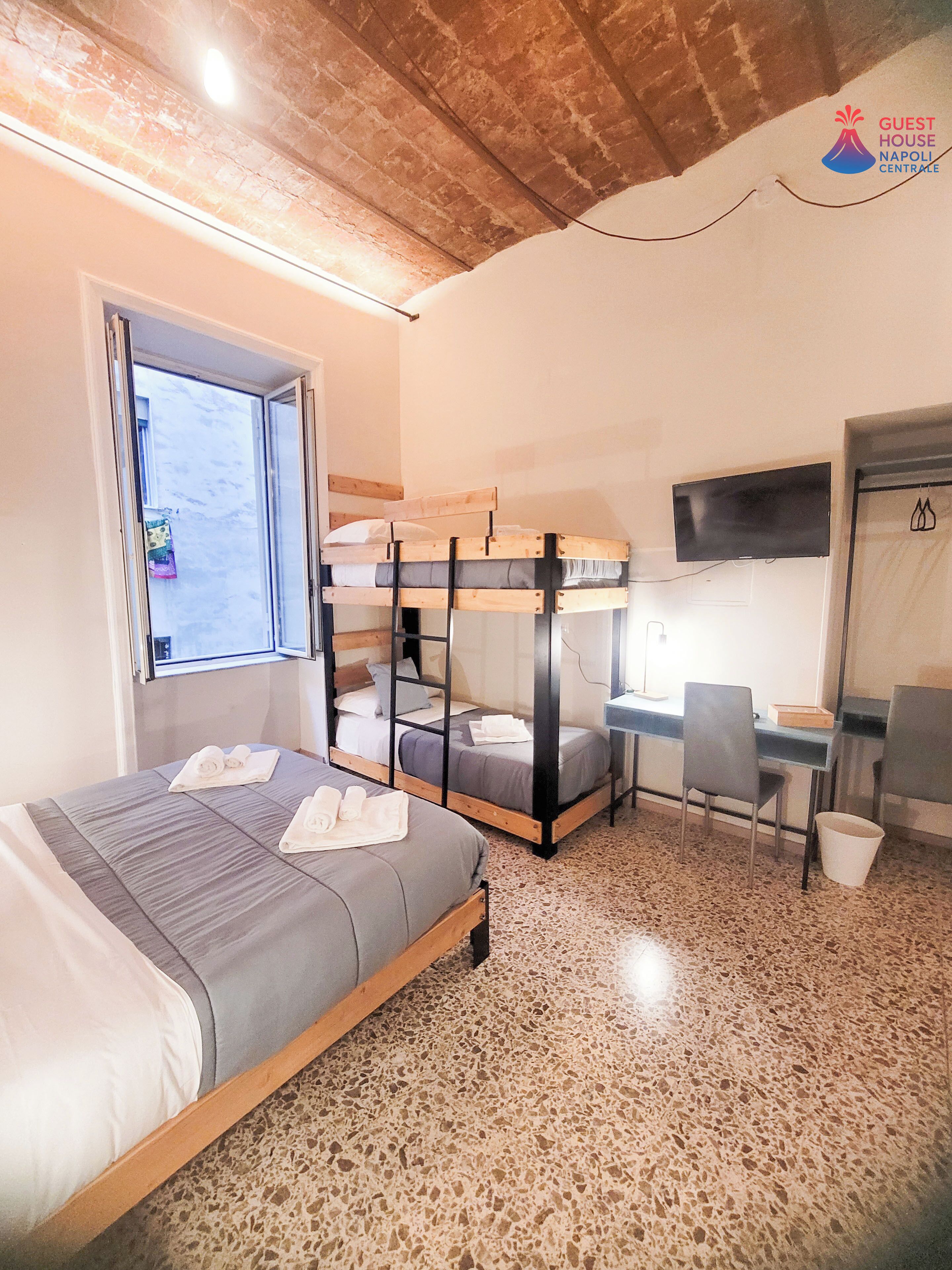 A room with a bunk bed, a desk with a chair, a TV, and a window.