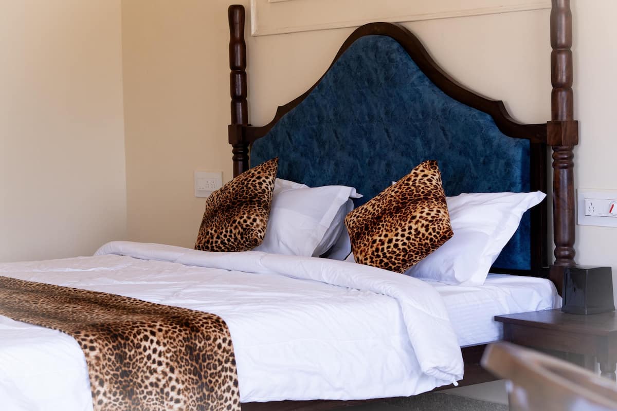 Een bed met een houten hoofdbord, witte beddengoed en twee kussens met luipaardprint.