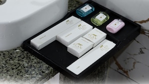 Un meuble-vasque de salle de bain sur lequel repose un plateau noir contenant divers articles de toilette, notamment une trousse de soins dentaires, une trousse de rasage et un bonnet de douche.
