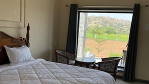 Une chambre avec un grand lit, une petite table, deux chaises et une vue sur un vignoble par la fenêtre.