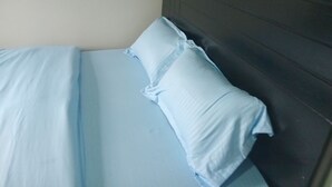 Een bed met een donker hoofdbord en lichtblauwe beddengoed.