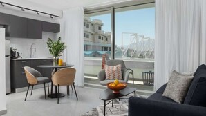A modern apartment with a kitchen, dining area, and living room. It features a large balcony with a view of buildings and a bridge. - דירת סטודיו עם מרפסת במתחם סי סייד -By Edomlux (Eilat)