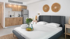A modern bedroom with a large bed, a small kitchen area, and two decorative wall pieces. - By Edomlux סטודיו מודרנית במתחם סי סייד 100 מטר מהים (Eilat)