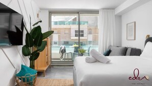 A hotel room with a bed, a TV, a large window, and a view of a building and a pool. - סוויטה יוקרתית במתחם סי סייד על הים - By Edomlux (Eilat)