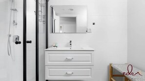 A modern bathroom with a glass shower enclosure, a white vanity with two drawers, a mirror, and a small wooden bench. - דירה משפחתית מעוצבת בסי סייד עם בריכה מחוממת - By Edomlux (Eilat)