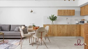 Un salon moderne avec un canapé gris, une table à manger avec des chaises et un coin cuisine doté de meubles en bois et d’un four à micro-ondes.