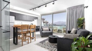 En moderne stue med sofa, spisebord med stole og en stor skydedør, der fører ud til en balkon med udsigt over by og bjerglandskab.