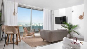 Een moderne woonkamer met een bank, een eethoek met stoelen, een aan de muur bevestigde televisie en een uitzicht over de stad door grote ramen.