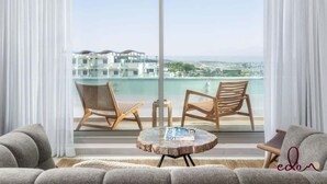 Een balkon met twee rieten stoelen, een ronde houten tafel met tijdschriften, en uitzicht op gebouwen aan de overkant van het water.
