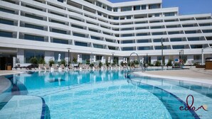 Ein modernes Hotel mit einem großen Schwimmbad, mehreren Balkonen und Sitzgelegenheiten im Freien.
