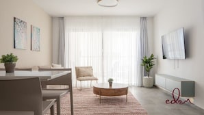 Uma sala de estar moderna com área de jantar, um sofá, uma mesa de centro e uma TV fixada na parede.