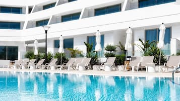 A swimming pool with lounge chairs and umbrellas, surrounded by a modern building with large windows.
