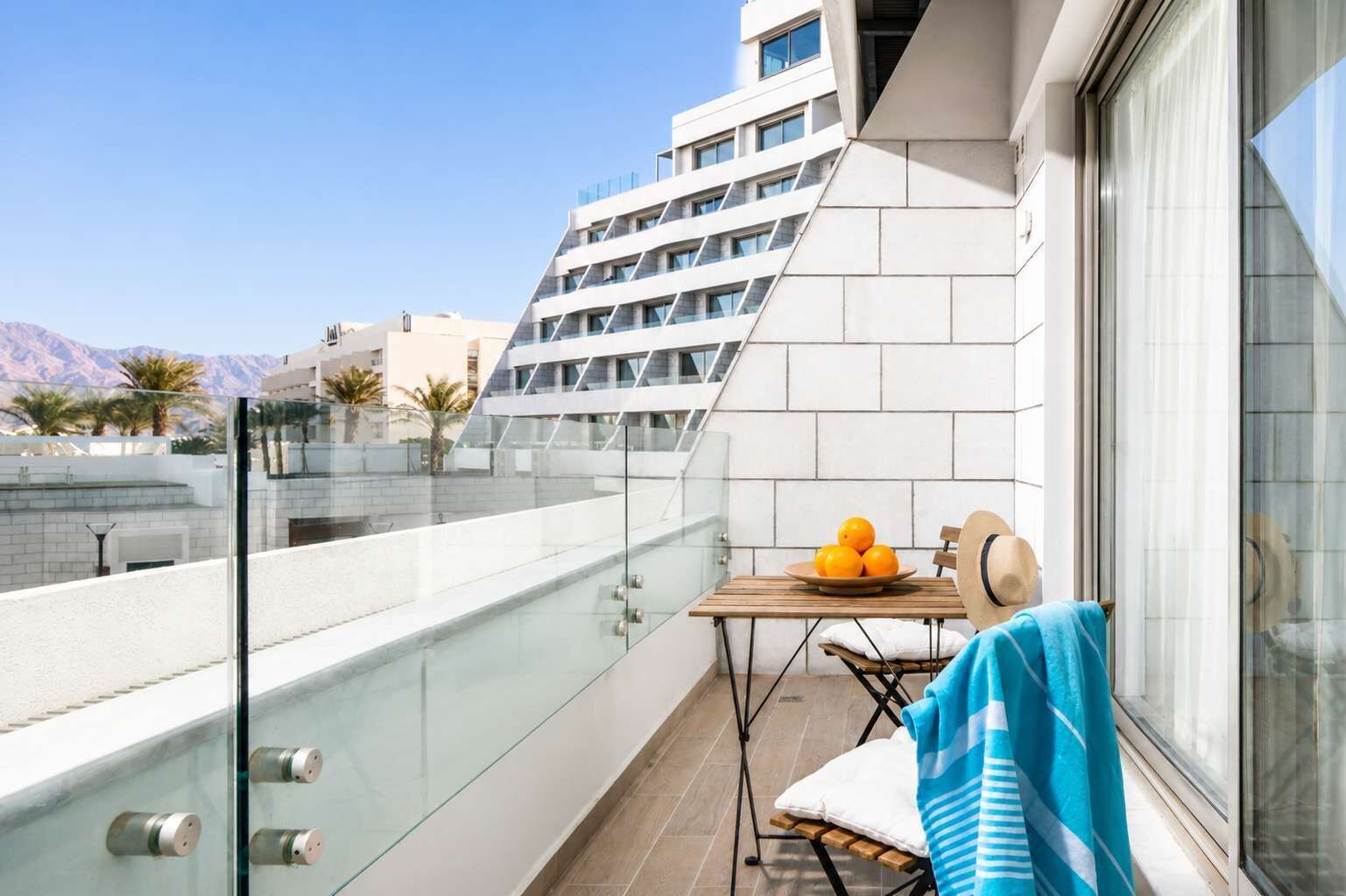 A balcony with a glass railing, a table with oranges, a chair, and a towel.