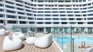 Un pont moderne de navire de croisière, doté d’un espace piscine, de chaises longues et d’une piscine à ciel ouvert protégée par des parois en verre.