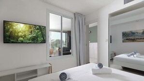Une chambre d’hôtel avec une grande télévision, un lit avec des serviettes, un banc et un tableau au mur.