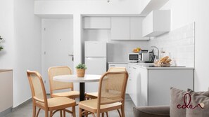 A modern kitchen with white cabinets, a round dining table with four wicker chairs, and a small island with a microwave and fruit bowl. - דירה משפחתית בסי סייד בריכה מחוממת - By Edomlux (Eilat)