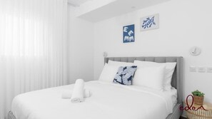 A hotel room with a neatly made bed, a small bedside table with a plant, and a wall with two pieces of artwork. - דירה משפחתית בסי סייד בריכה מחוממת - By Edomlux (Eilat)